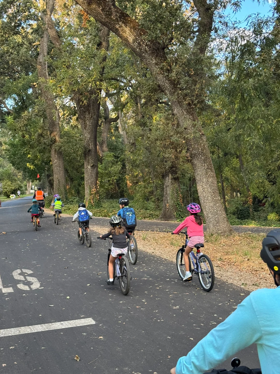 Young riders following an orange-vested rider along a shaded path