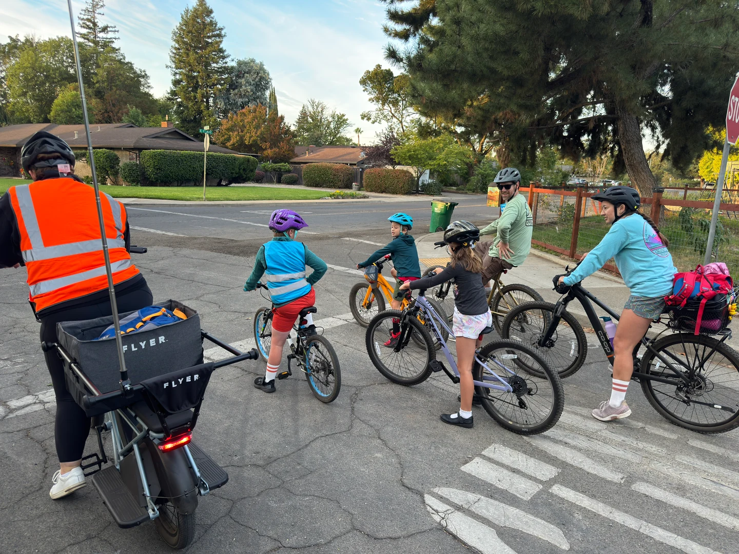 Helmeted riders waiting together at an intersection beside a cargo bike