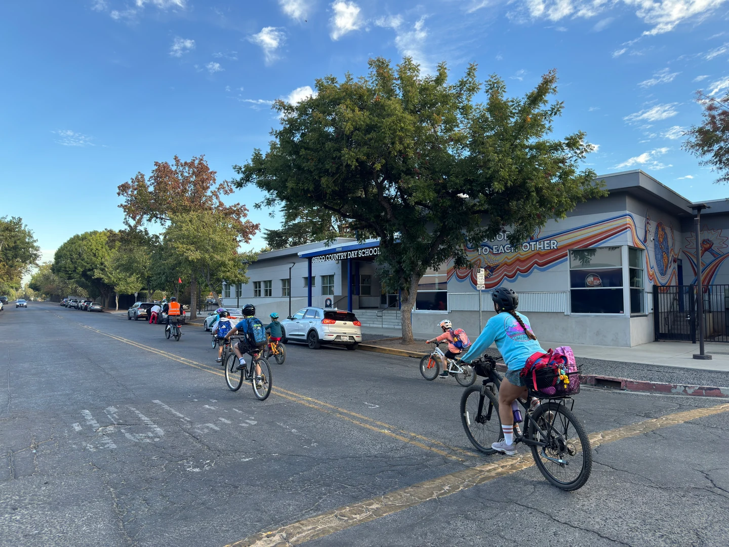 The bike group riding past a school building with a colorful mural